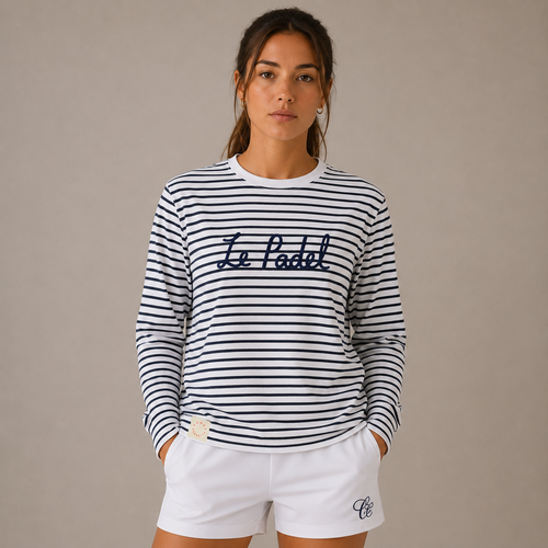 A woman modeling a navy and white horizontally striped long-sleeve t-shirt with 'Le Padel' embroidered across the chest, paired with white shorts, against a solid beige background.