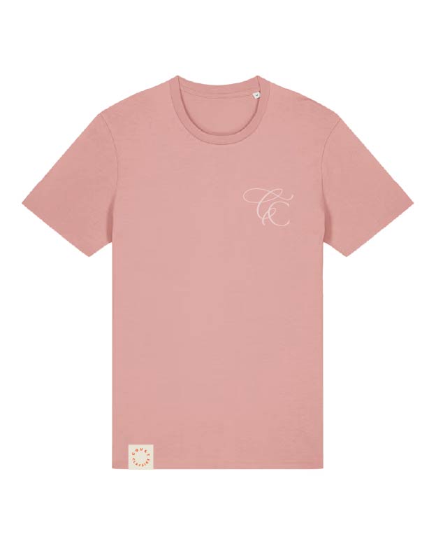 A dusty pink short-sleeve crewneck t-shirt with a small white cursive monogram logo on the left chest and a small square cream patch on the bottom left hem, shown against a plain white background.